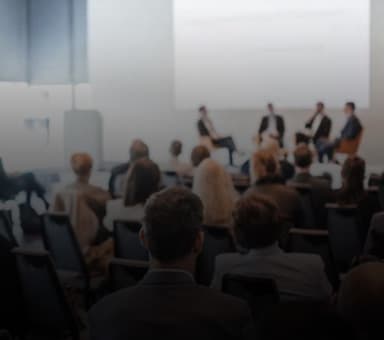 Eine Gruppe von Personen sitzt im Publikum und schaut auf eine Diskussionsrunde auf einer Bühne.